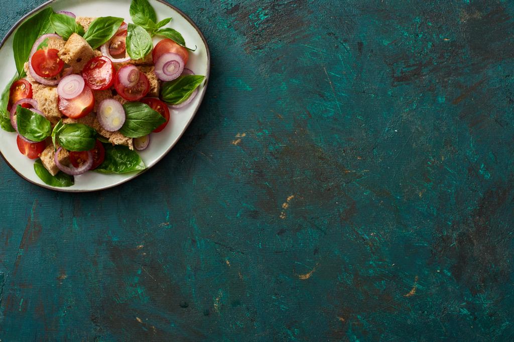 vista superior de la deliciosa ensalada de verduras italiana panzanella servido en el plato en la superficie verde texturizada
 - Foto, Imagen