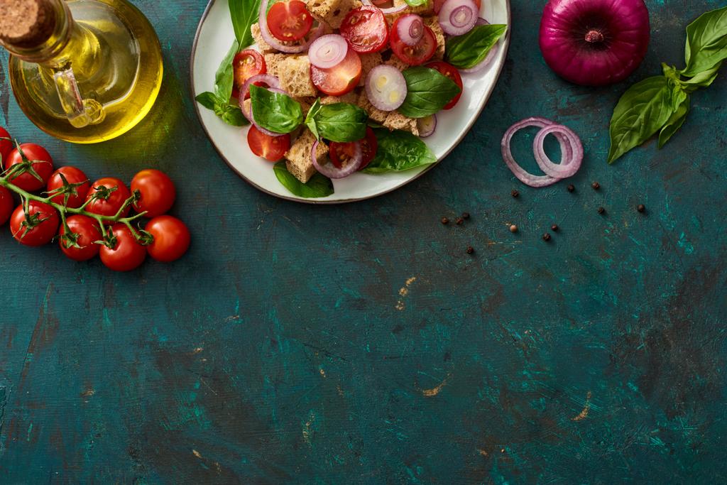 felülnézet ízletes olasz zöldségsaláta panzanella tálalva tányéron texturált zöld felületen összetevőkkel - Fotó, kép