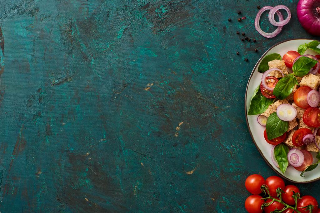 top view of delicious Italian vegetable salad panzanella served on plate on textured green surface with ingredients - 写真・画像