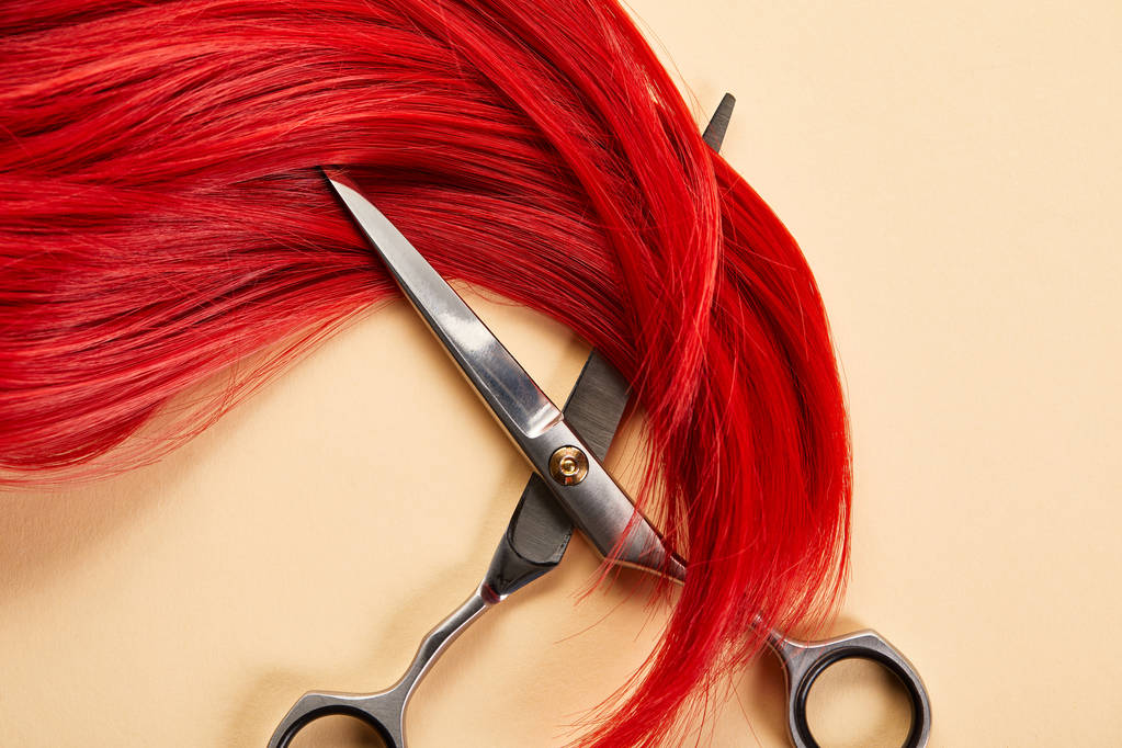 Draufsicht auf rote Haare und Schere auf beigem Hintergrund - Foto, Bild