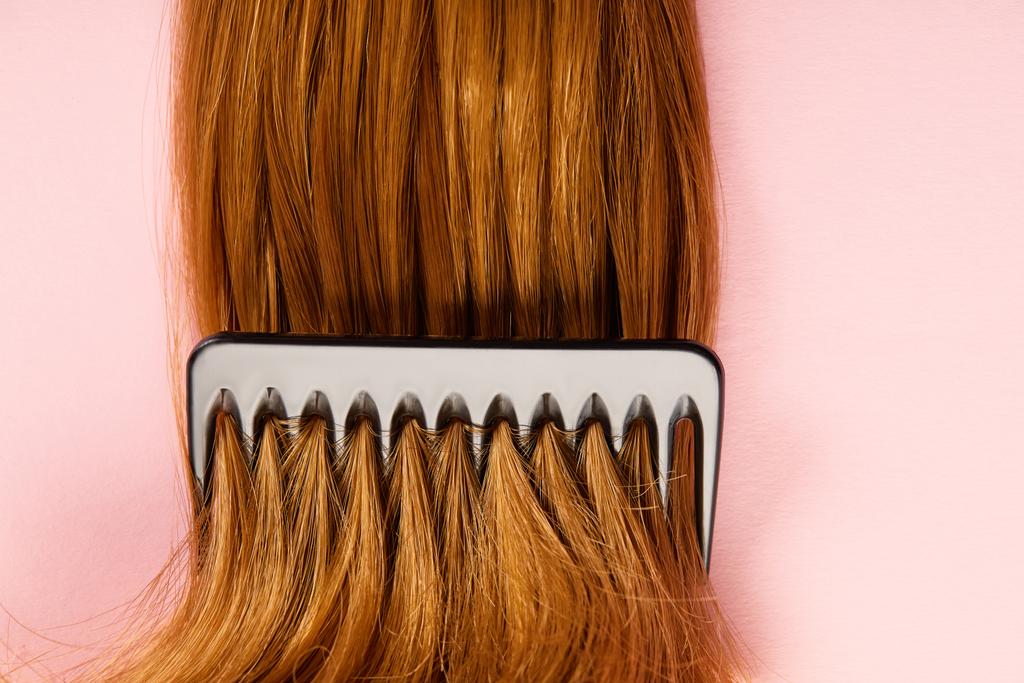 Top view of comb in brown hair on pink background - Photo, Image