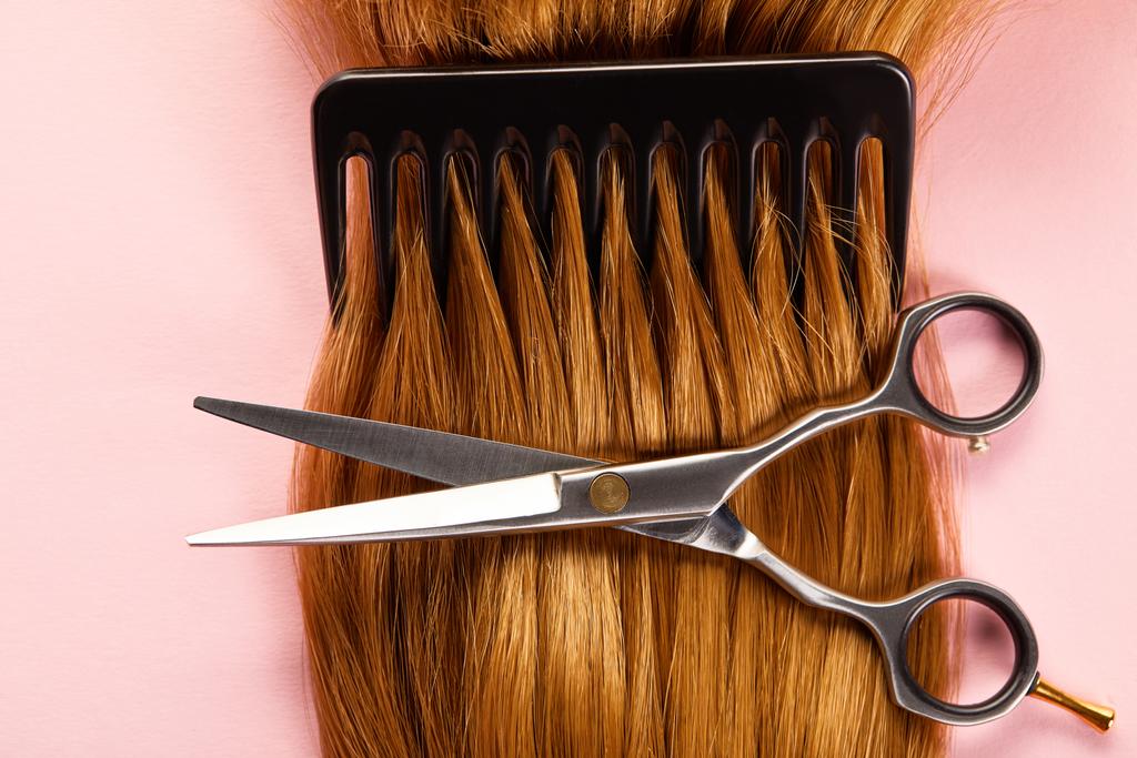Top view of scissors, comb and brown hair on pink background - Photo, Image