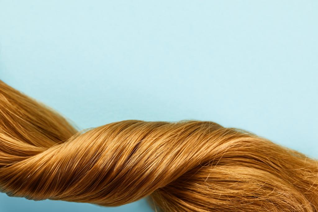Κάτοψη του στριμμένα καστανά μαλλιά απομονώνονται σε μπλε  - Φωτογραφία, εικόνα