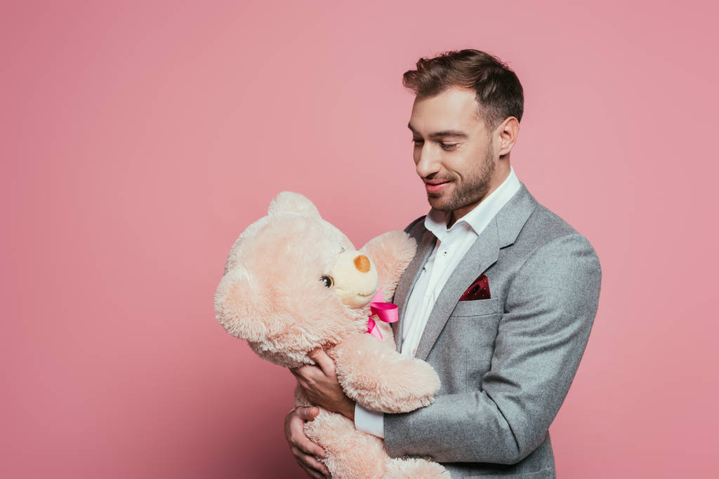 szakállas mosolygós férfi öltönyben kezében játékmackó, elszigetelt rózsaszín - Fotó, kép