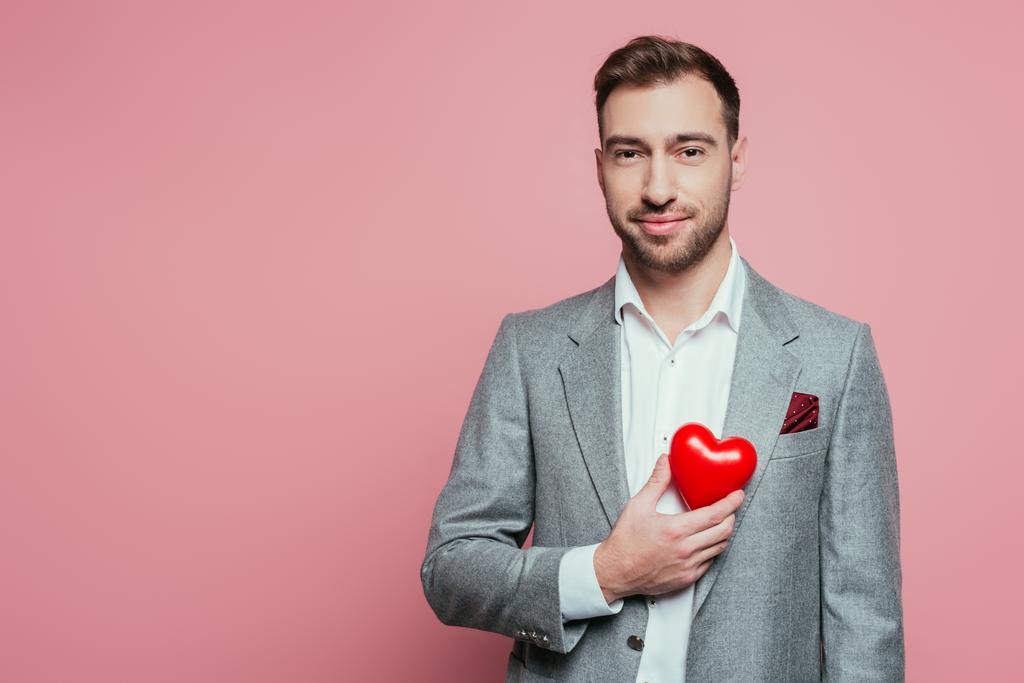schöner Mann mit rotem Herz zum Valentinstag, isoliert auf rosa  - Foto, Bild