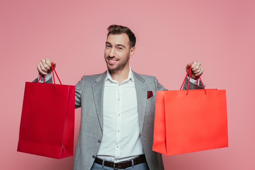 šťastný pozitivní muž drží nákupní tašky, izolované na růžové - Fotografie, Obrázek