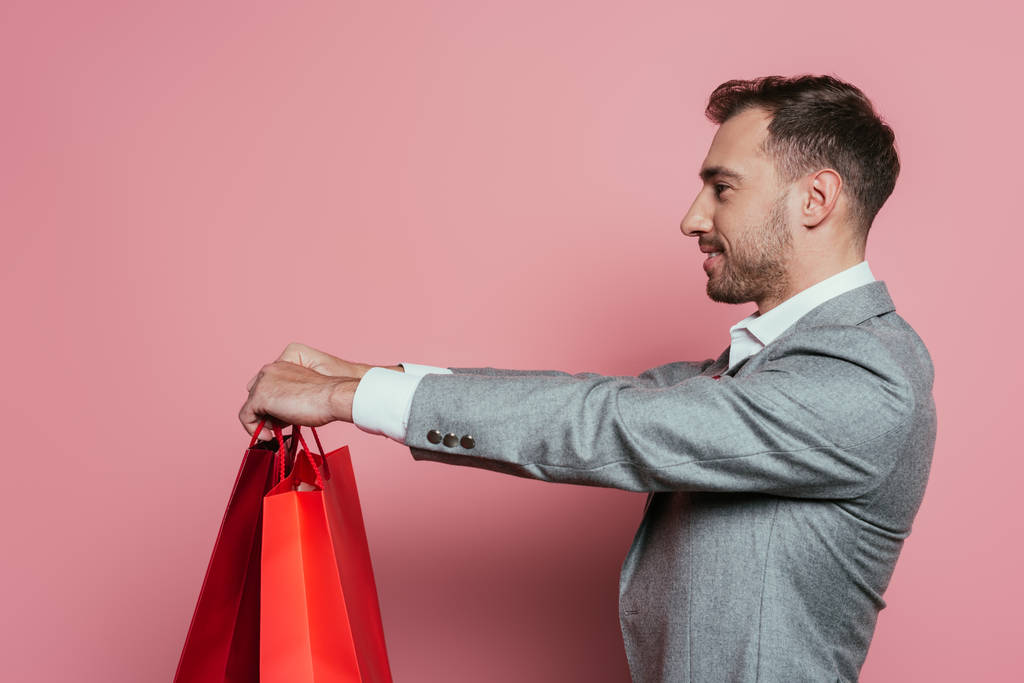 happy man holding shopping bags, isolated on pink - Photo, Image