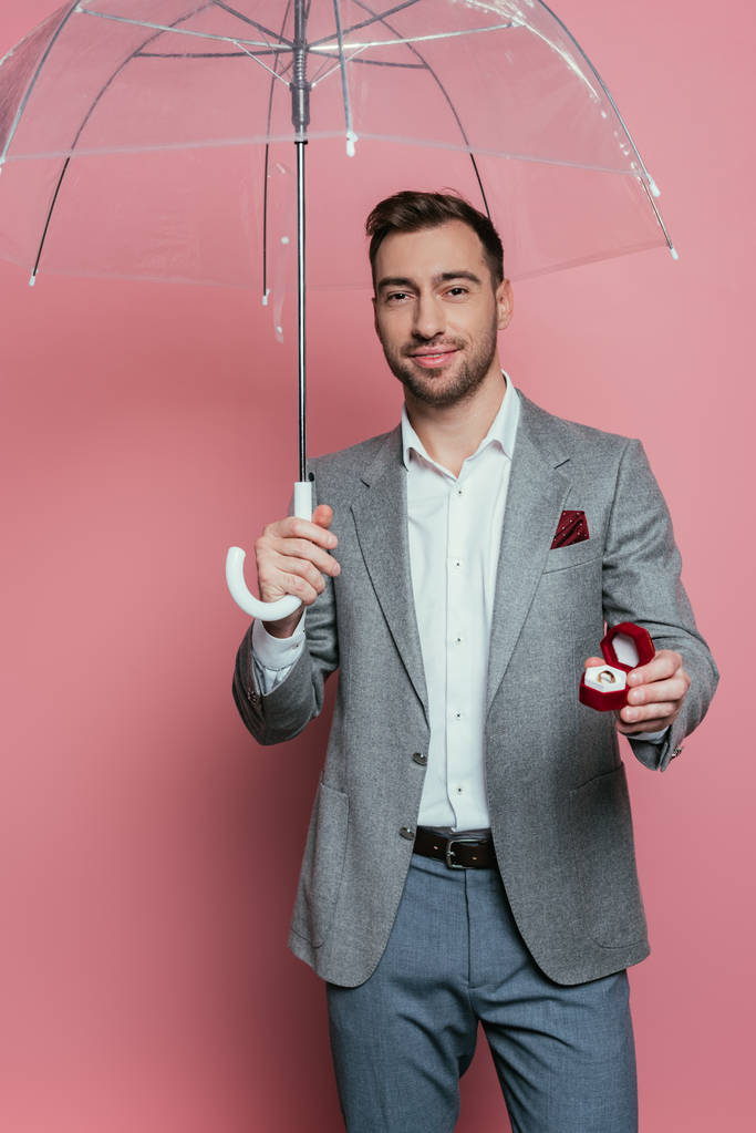 szczęśliwy człowiek gospodarstwa propozycja pierścień i parasol, izolowane na różowy  - Zdjęcie, obraz