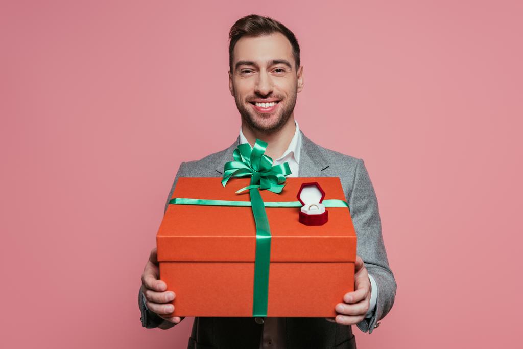 glimlachende man met groot cadeau en aanzoek ring, geïsoleerd op roze - Foto, afbeelding