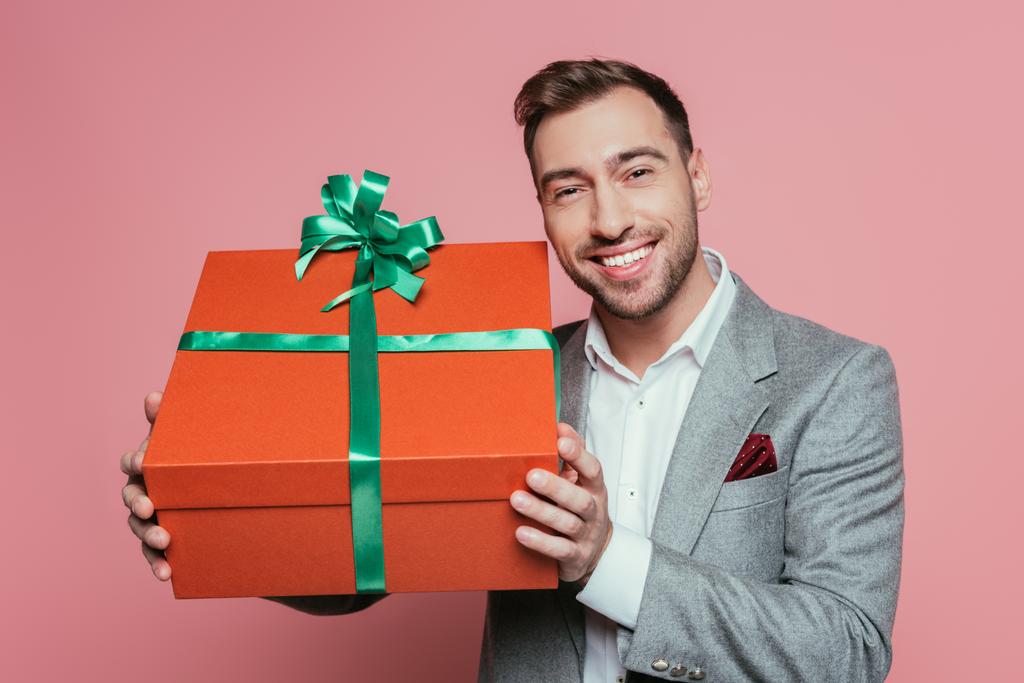 hombre positivo en traje que sostiene la caja de regalo grande, aislado en rosa
 - Foto, imagen