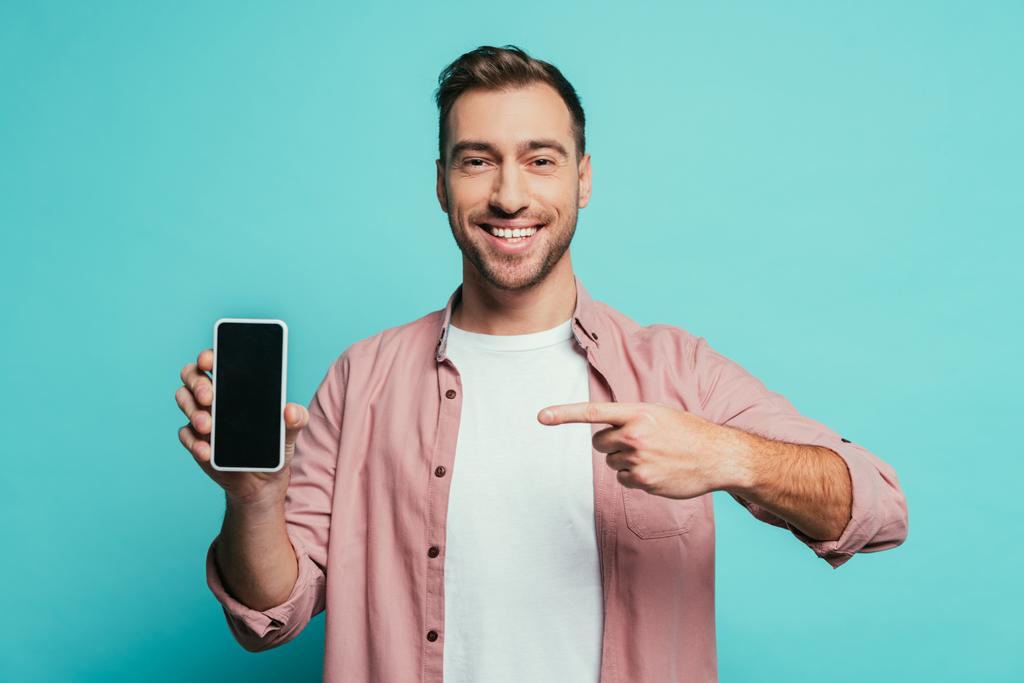 smiling man pointing at smartphone with blank screen, isolated on blue - Photo, Image
