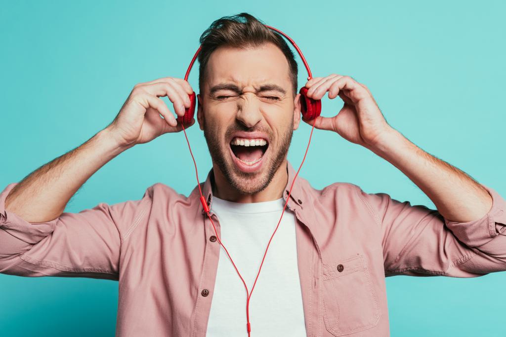 ενθουσιασμένοι άνθρωπος φωνάζοντας και ακούγοντας μουσική με ακουστικά, απομονώνονται σε μπλε - Φωτογραφία, εικόνα