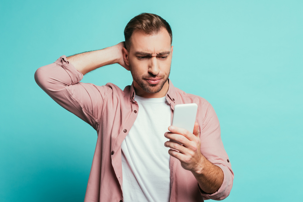 hombre guapo confundido usando teléfono inteligente, aislado en azul
 - Foto, Imagen