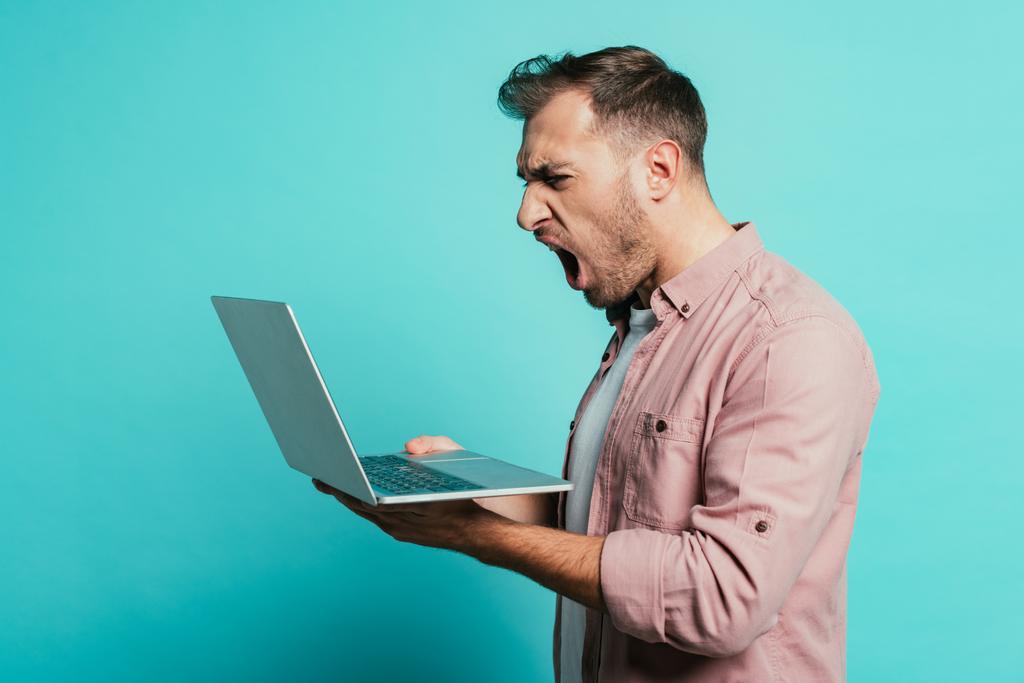 aggressive bearded man yelling at laptop, isolated on blue - Photo, Image