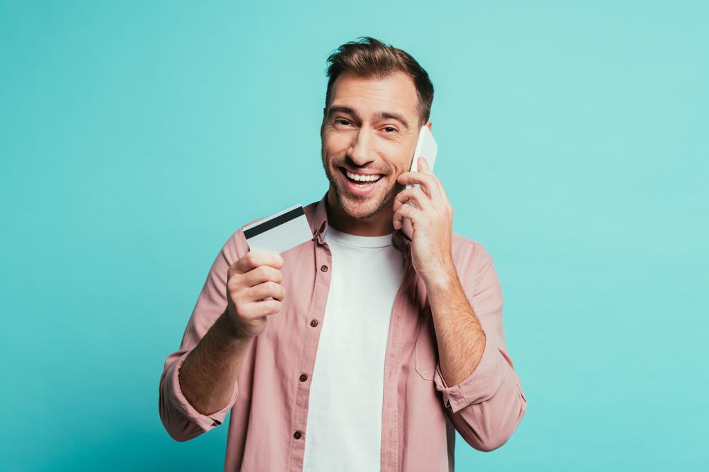 усміхнений чоловік купує онлайн зі смартфоном та кредитною карткою, ізольовані на синьому
 - Фото, зображення