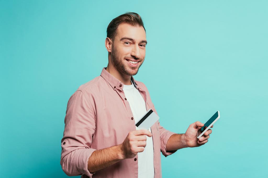 homem barbudo alegre compras on-line com smartphone e cartão de crédito, isolado no azul
 - Foto, Imagem