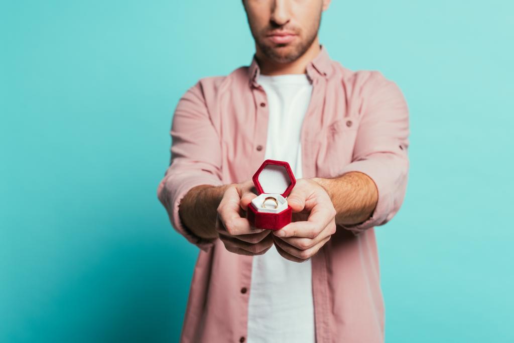vágott kilátás komoly férfi holding box eljegyzési gyűrű, elszigetelt kék - Fotó, kép