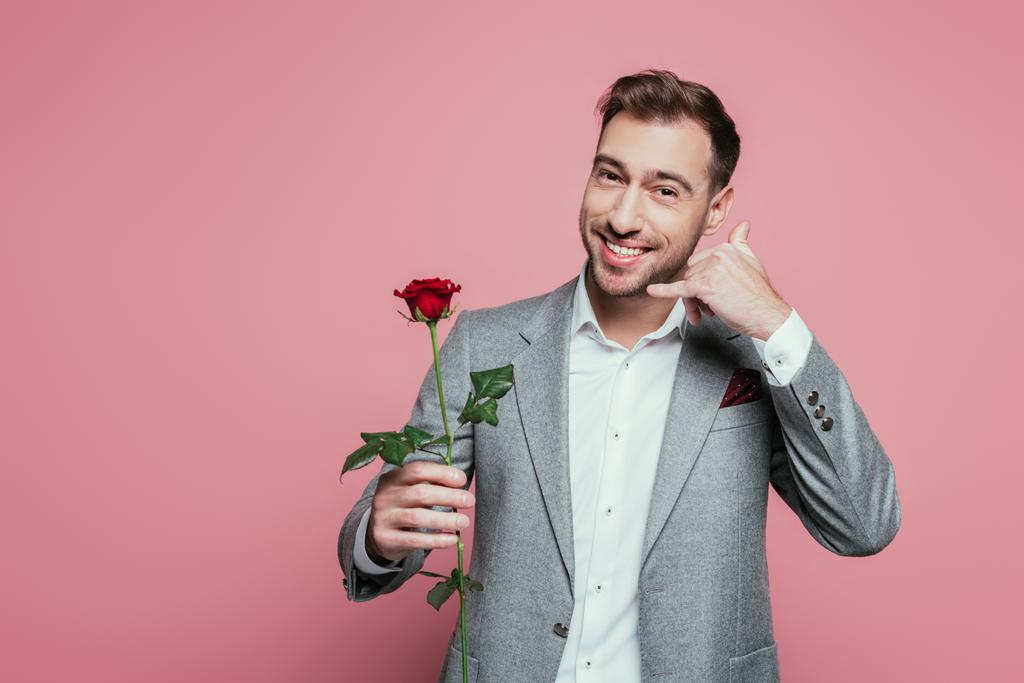 vidám férfi kezében rózsa és mutatja hív gesztus, elszigetelt rózsaszín - Fotó, kép