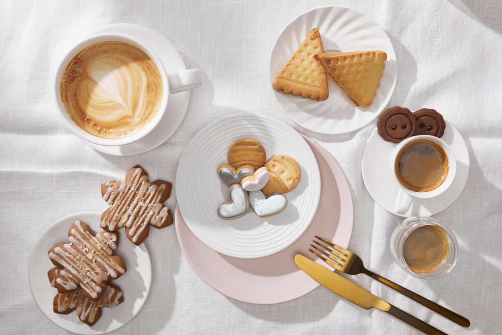 Draufsicht auf leckere Kekse mit Glasur und Kaffee auf weißer Tischdecke - Foto, Bild