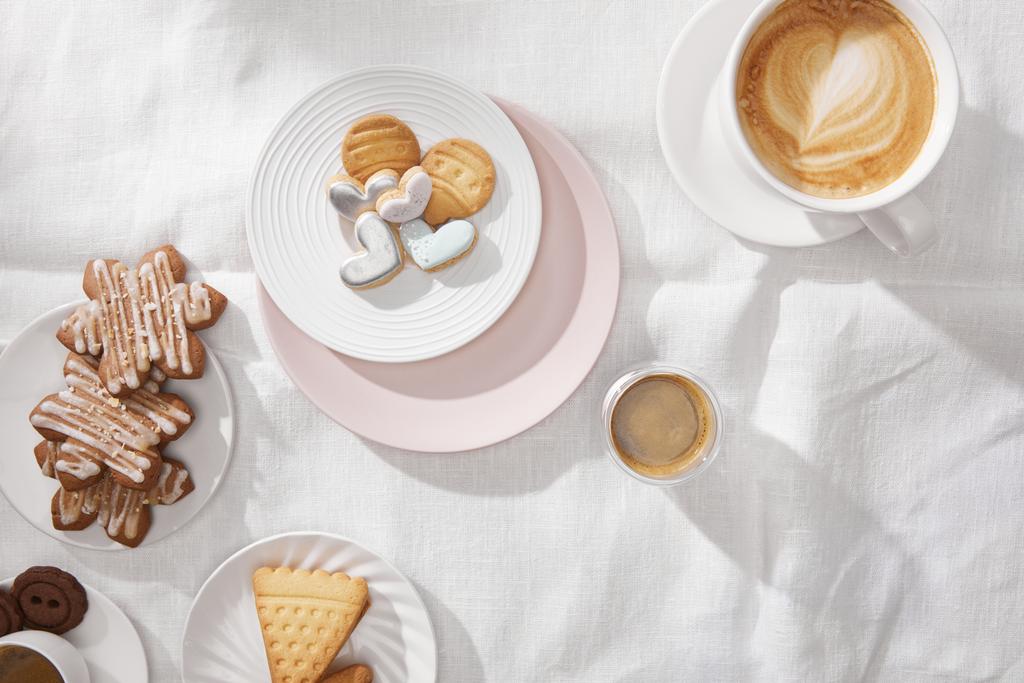 Horní pohled na cookies s glazurou a šálky kávy na bílém ubrusu - Fotografie, Obrázek