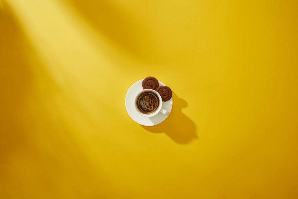 Κάτοψη γευστικών μπισκότων σε πιατάκι του φλιτζανιού του καφέ σε κίτρινο φόντο - Φωτογραφία, εικόνα