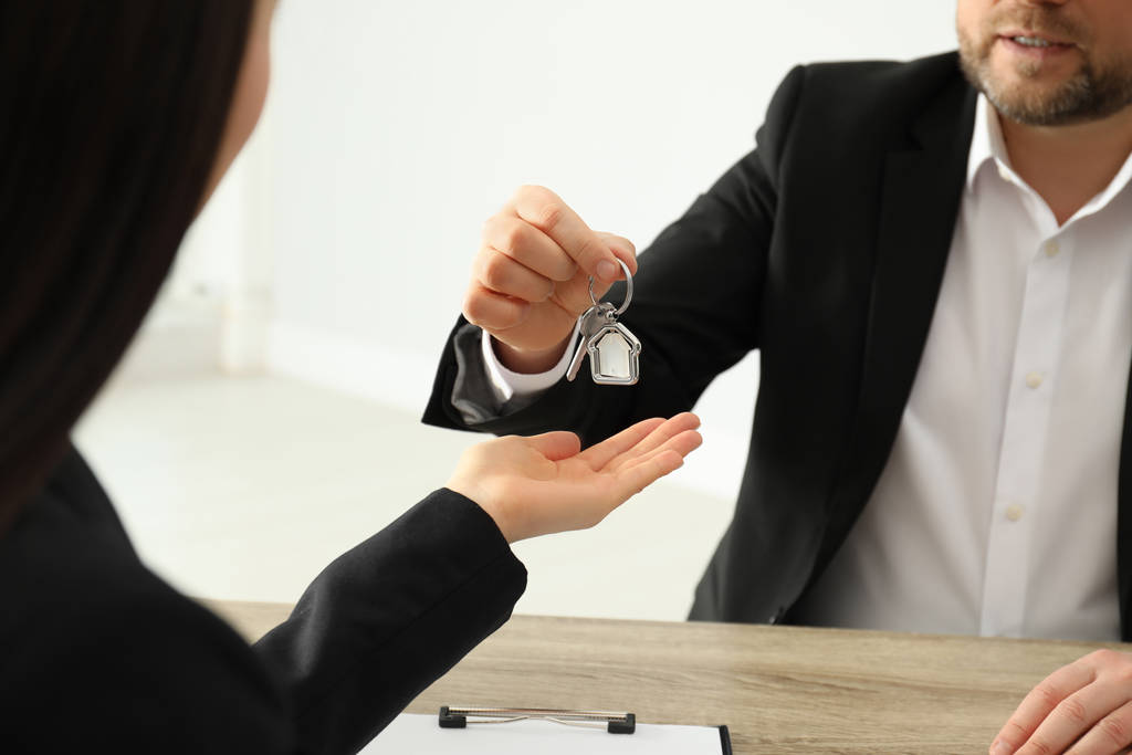 Agente de bienes raíces dando la llave al cliente en la mesa en la oficina, cerca
 - Foto, Imagen