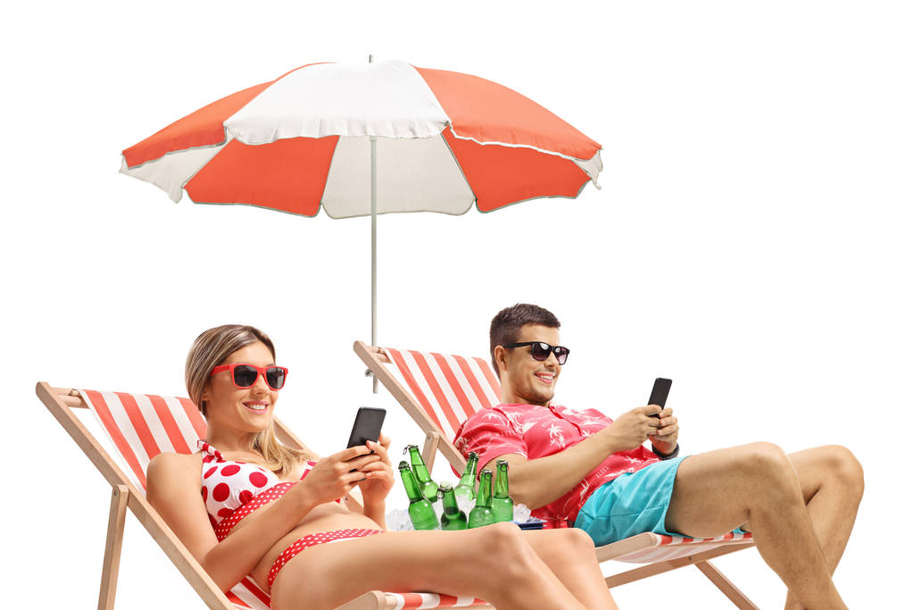 Jongeman en vrouw met telefoons zonnebaden in ligstoelen - Foto, afbeelding