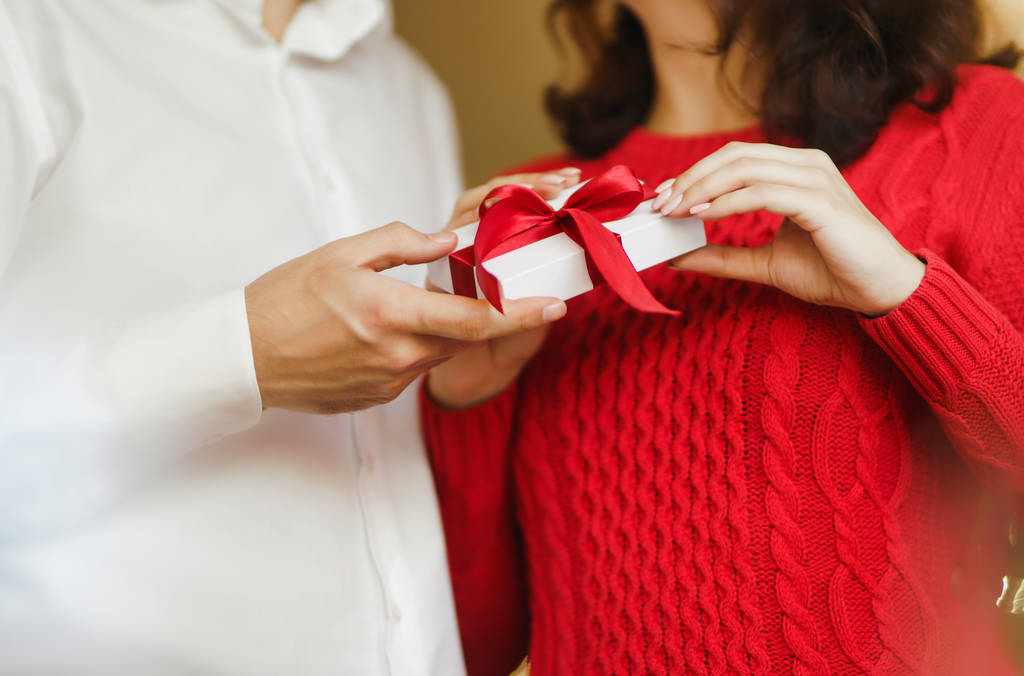Valentine's Day, holiday and surprise concept. Man gives to his woman a gift box with red ribbon. A loving couple cuddles and celebrating Valentine's Day in the restaurant. Lovers give each other gift - Photo, Image