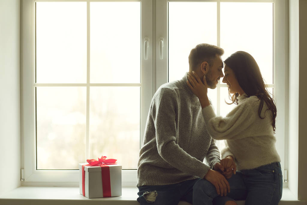 Vista trasera de una joven pareja sentada en un alféizar de la ventana mirando por la ventana. Día de San Valentín
. - Foto, imagen