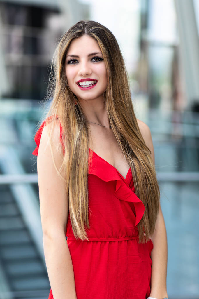Красивая женщина в красном платье улыбается на открытом воздухе - Фото, изображение