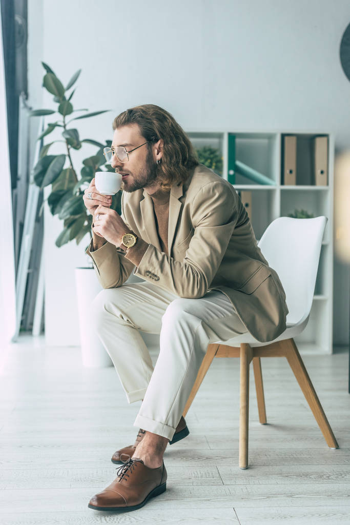eleganter Geschäftsmann trinkt Kaffee auf Stuhl im Büro - Foto, Bild