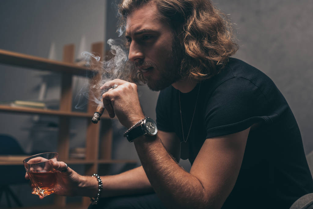 μοντέρνος επιχειρηματίας με μαύρα ρούχα καπνίζει πούρο και πίνει ουίσκι  - Φωτογραφία, εικόνα