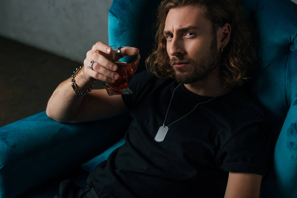fashionable businessman in black outfit holding glass of whiskey in armchair - Photo, Image