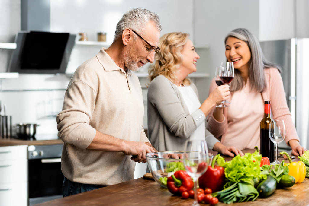 усміхнена мультикультурна жінка смердить і чоловік ріже салат на кухні
  - Фото, зображення