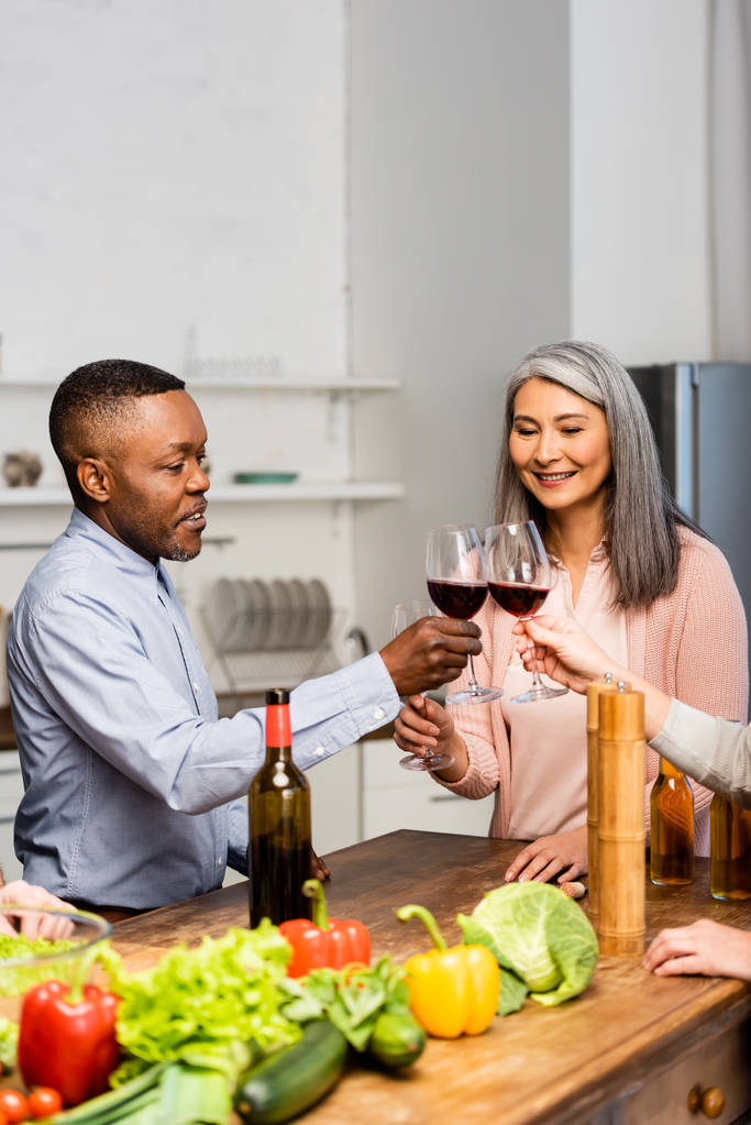 bijgesneden weergave van glimlachende multiculturele vrienden klinkend met wijnglazen  - Foto, afbeelding