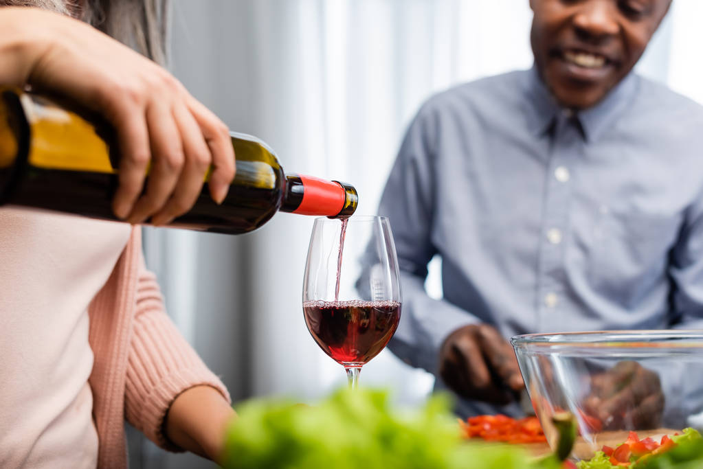 cropped view of woman pouring wine to glass and african american man looking at it  - Photo, Image