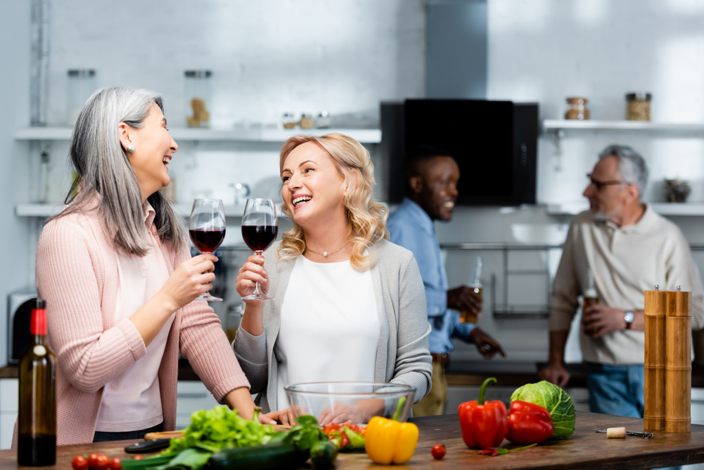 szelektív fókusz mosolygós multikulturális barátok kezében borospoharak a konyhában  - Fotó, kép
