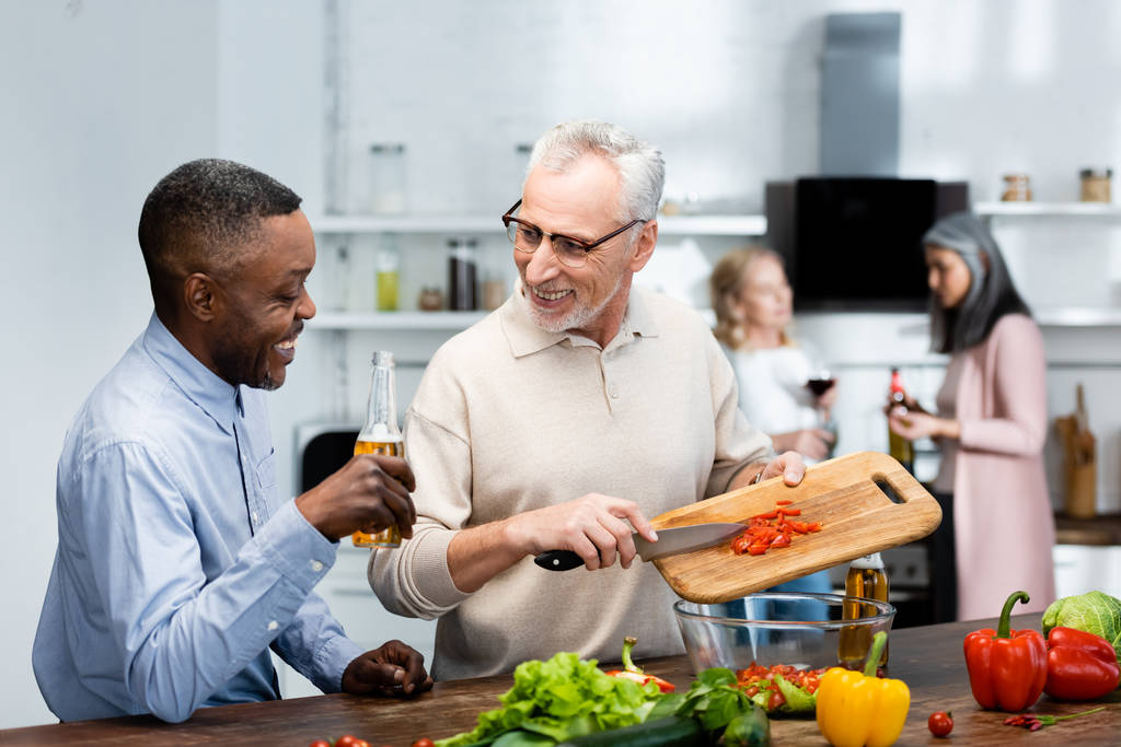 Afrikanisch-amerikanischer Mann hält Bier und sein Freund fügt Kirschtomaten zum Salat hinzu  - Foto, Bild