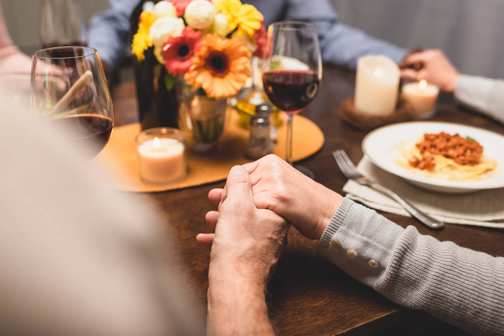 abgeschnittene Ansicht eines Mannes, der die Hand eines Freundes hält und während des Abendessens betet  - Foto, Bild