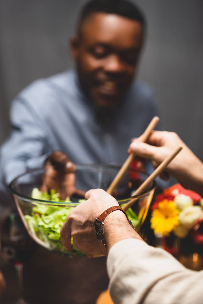 обрезанный вид женщины, дающей миску с салатом африканской американской подруге во время ужина
  - Фото, изображение