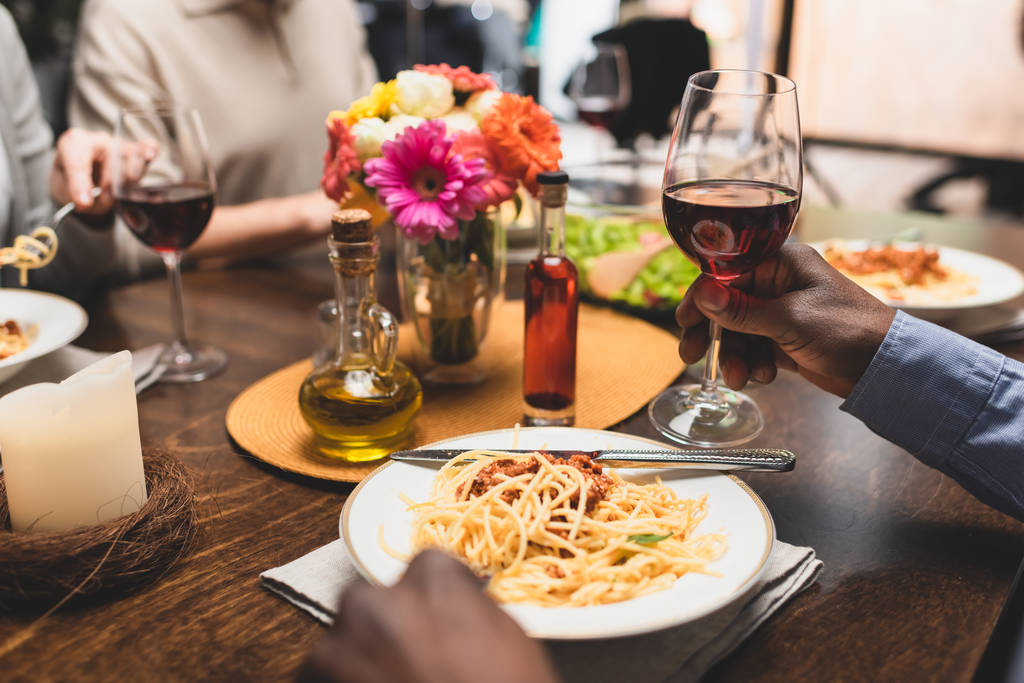 vista recortada del hombre afroamericano sosteniendo copa de vino durante la cena
  - Foto, Imagen