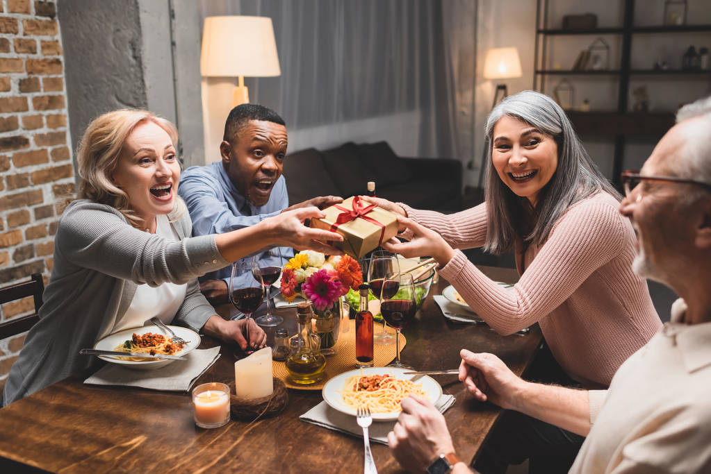 mosolygó multikulturális barátok kezében ajándék és nézi az ember vacsora közben  - Fotó, kép