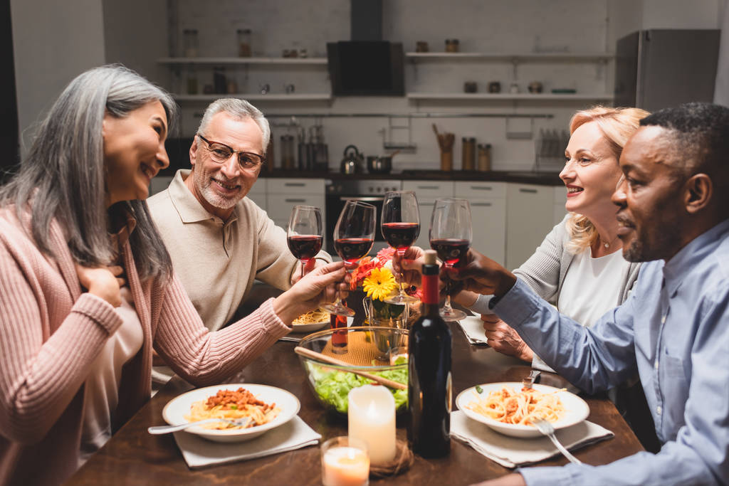 Gülümseyen çok kültürlü arkadaşlar yemek boyunca şarap kadehleriyle çakışıyorlar.  - Fotoğraf, Görsel