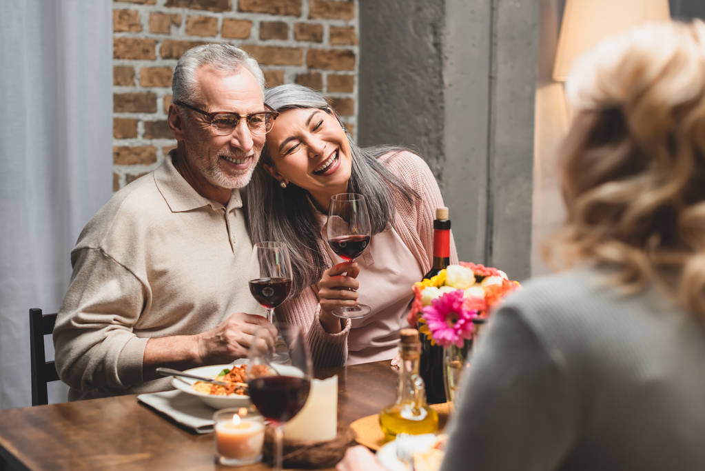 focus selettivo di sorridenti amici multiculturali che tengono bicchieri di vino durante la cena
  - Foto, immagini