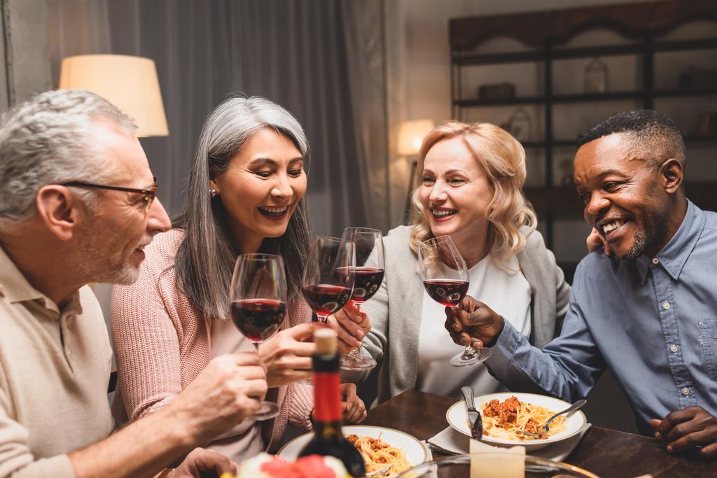 Gülümseyen çok kültürlü arkadaşlar yemek boyunca şarap kadehleriyle konuşur ve şıngırdarlar.  - Fotoğraf, Görsel