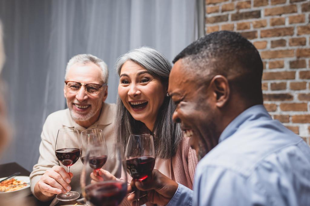 souriant amis multiculturels parler et tenir des verres à vin pendant le dîner
  - Photo, image