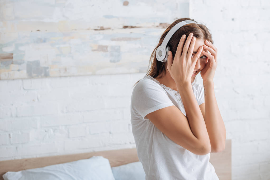 cheerful woman covering face while smiling and listening music at home  - Photo, Image
