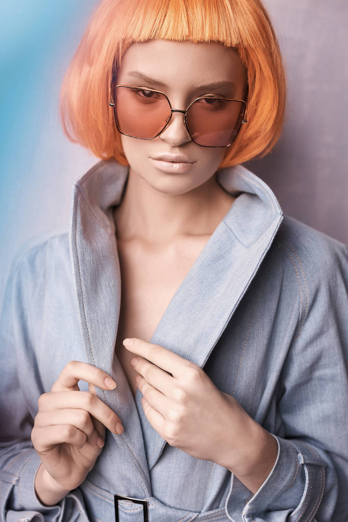 портрет красивой девушки в оранжевых очках на розовом фоне с голым макияжем и короткими оранжевыми волосами она одета в джинсовую куртку и смотрит в камеру
 - Фото, изображение