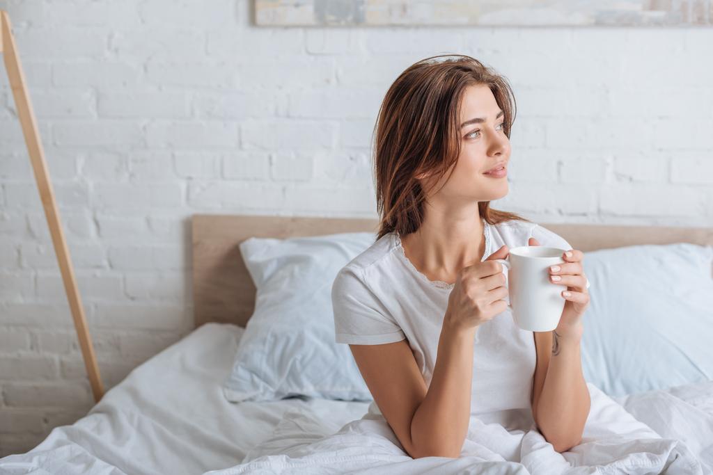 gelukkig jong vrouw holding cup met thee in slaapkamer  - Foto, afbeelding