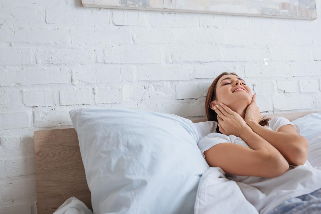 glückliche Frau berührt Hals beim Träumen und Liegen im Bett  - Foto, Bild